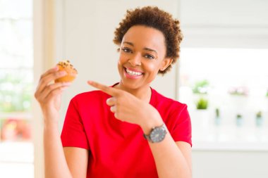 Genç Afro-Amerikan kadın yeme çikolata muffins el ve parmak ile işaret çok mutlu fişleri