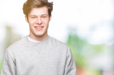 Yüz üzerinde mutlu ve serin bir gülümseme ile izole arka plan üzerinde sweatshirt giyen genç yakışıklı sportif adam. Şanslı kişi.