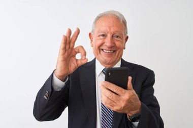 Üst düzey gri saçlı işadamı parmakları ile ok işareti yapıyor izole beyaz arka plan üzerinde duran akıllı telefon kullanarak, mükemmel sembolü