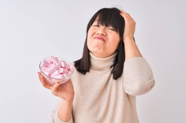 Izole beyaz arka plan üzerinde marshmallows ile kase tutan güzel Çinli kadın baş el ile vurguladı, utanç ve sürpriz yüz ile şok, kızgın ve sinirli. Korku ve hata için üzgün.