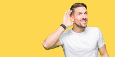 Casual beyaz t-shirt el ile bir işitme söylenti ya da dedikodu için dinleme kulak üzerinde gülümseyen giyen yakışıklı adam. Sağırlık kavramı.