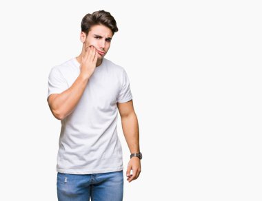 Diş ağrısı veya dişlerde dişlerle ilgili hastalık nedeniyle ağız acı ifadesi ile el ile dokunmak izole arka plan üzerinde beyaz t-shirt giyen genç yakışıklı adam. Diş hekimi kavramı.