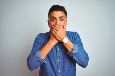 İzole beyaz arka plan üzerinde ayakta kot gömlek giyen genç Brezilyalı adam yanlışlık için eller ile ağız kapsayan şok. Gizli konsept.