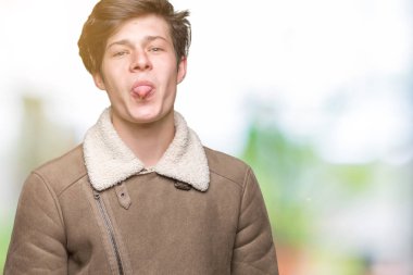 Genç yakışıklı adam izole arka plan üzerinde kış ceket giyiyor komik ifade ile mutlu dil dışarı yapışması. Duygu konsepti.