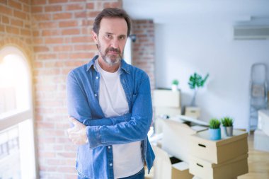 Orta yaş kıdemli adam yeni bir ev ambalaj karton kutular şüpheci ve sinir, çapraz silah ile yüz üzerinde ifade onaylanmaya hareket. Negatif kişi.