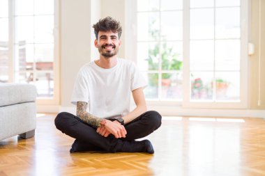 Genç adam yüz üzerinde mutlu ve serin bir gülümseme ile evde yerde rahat oturan çalışıyor. Şanslı kişi.