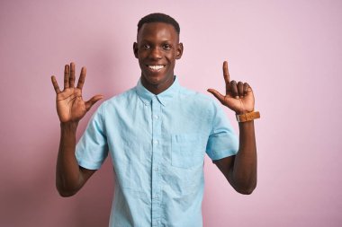 Afrika Amerikan adam izole pembe arka plan üzerinde ayakta mavi rahat gömlek giymiş ve parmak sayısı yedi ile işaret kadar emin ve mutlu gülümseyen.