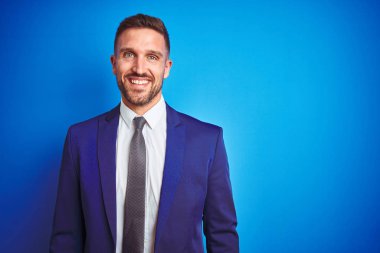 Yüzünde mutlu ve serin bir gülümseme ile mavi izole arka plan üzerinde genç yakışıklı iş adamı. Şanslı kişi.