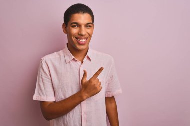 Genç yakışıklı arap adam izole pembe arka plan neşeli üzerinde duran rahat gömlek giyen yüzünde mutlu ve doğal ifade ile yan yana el ve parmak ile işaret eden yüz bir gülümseme ile neşeli