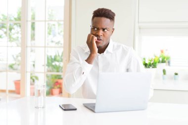 Afro-Amerikan iş adamı dizüstü bilgisayar kullanarak çalışan stresli ve ağız tırnak ısırma elleri ile sinirli görünümlü. Anksiyete sorunu.