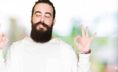 Uzun saçlı ve sakal giyen sportif Sweatshirt ile genç adam Relax ve gözleri ile gülümseyen meditasyon jest parmaklar ile kapalı. Yoga konsepti.