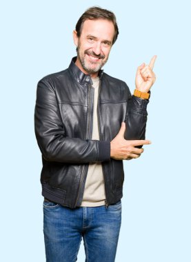 Yüzünde büyük bir gülümseme ile siyah deri ceket giyen orta yaş yakışıklı adam, kamera bakarak yan el ve parmak ile işaret.