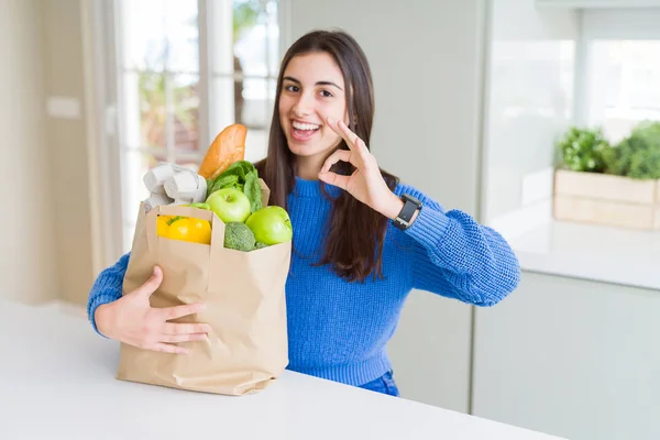 健康的な食料品でいっぱいの紙袋を持つ美しい若い女性は 指でOkサインを行い 優れたシンボル — ストック写真