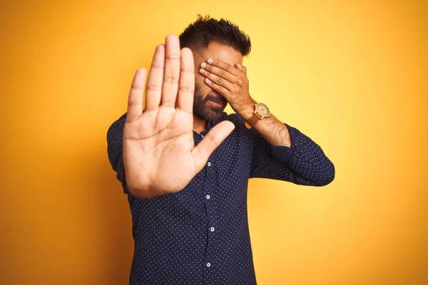 Young handsome indian businessman wearing shirt over isolated yellow background covering eyes with hands and doing stop gesture with sad and fear expression. Embarrassed and negative concept.