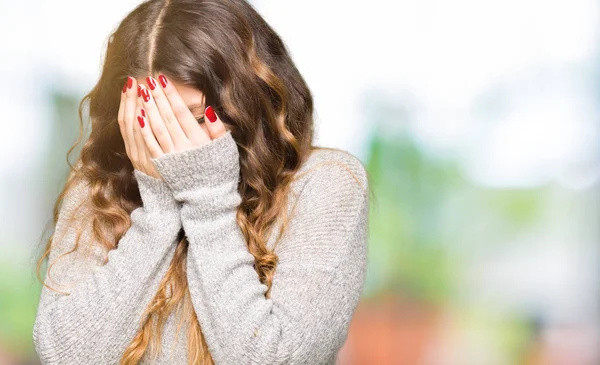 Young beautiful woman wearing winter dress with sad expression covering face with hands while crying. Depression concept.