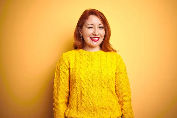 美丽的红发女人穿着冬季毛衣站在孤立的黄色背景眨眼看相机性感的表情 欢快和快乐的脸 — 图库照片