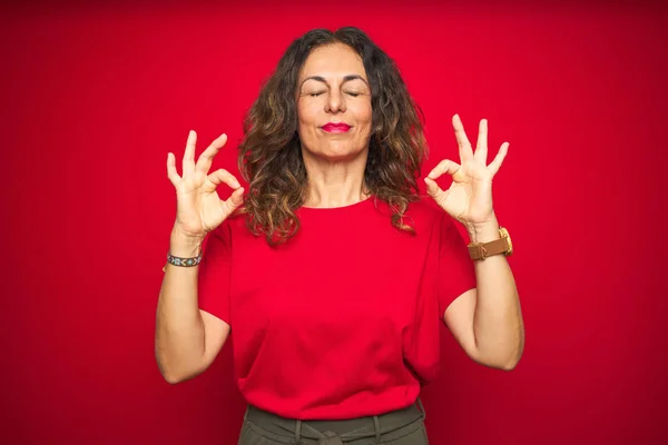 赤い孤立した背景の上に巻き毛を持つ中年のシニア女性はリラックスし 指で瞑想ジェスチャーをして目を閉じて微笑んでいます ヨガのコンセプト — ストック写真