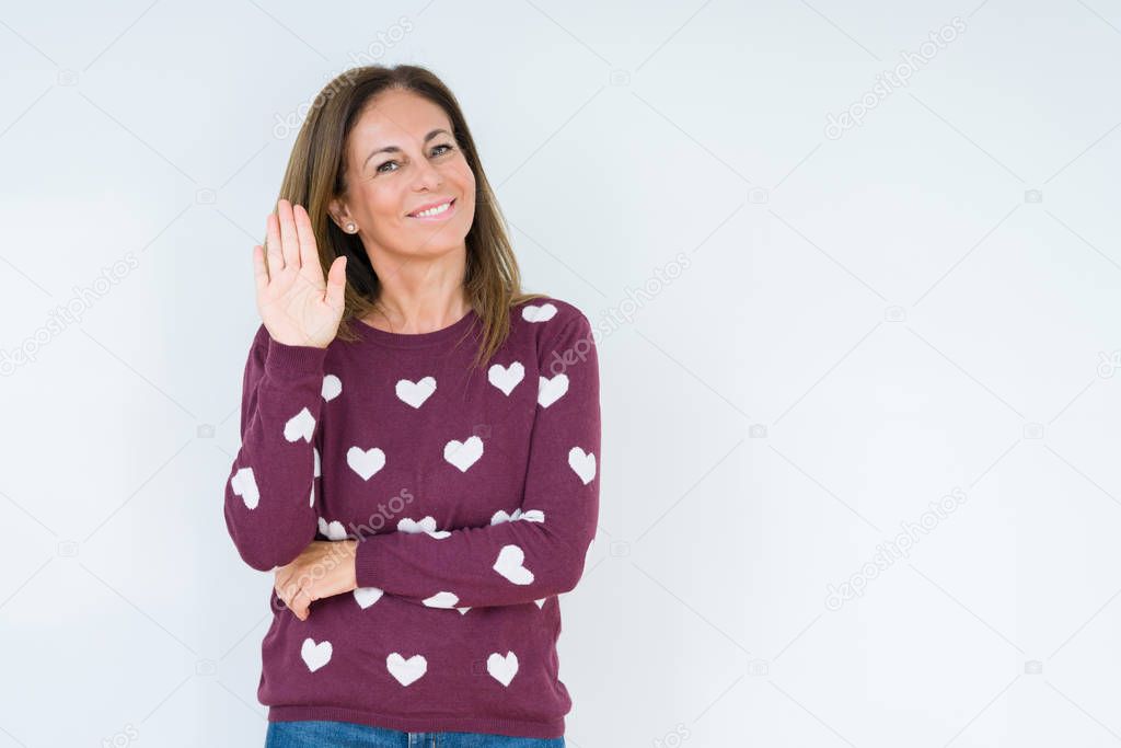 Beautiful middle age woman wearing heart sweater over isolated background Waiving saying hello happy and smiling, friendly welcome gesture