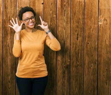 Genç güzel Afrikalı-Amerikalı kadın gözlük gösterilen ve parmakları ile işaret izole arka plan üzerinde kendinden emin ve mutlu gülümseyerek süre yedi numara.