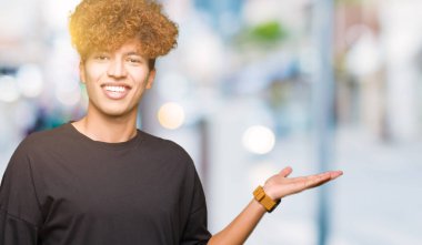 Neşeli sunulması ve kameraya bakarak avucunun ile işaret gülümseyen siyah t-shirt giyen afro saçlı genç yakışıklı adam.