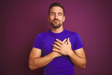 Lila izole arka plan üzerinde rahat mor t-shirt giyen genç adam gözleri kapalı gözler ve yüz minnettar jest ile göğsüne el ile gülümsüyor. Sağlık konsepti.