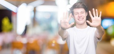 Yakışıklı delikanlı gösterilen ve parmakları ile işaret izole arka plan üzerinde rahat beyaz t-shirt giyen numara 9 kendinden emin ve mutlu gülümseyerek süre.