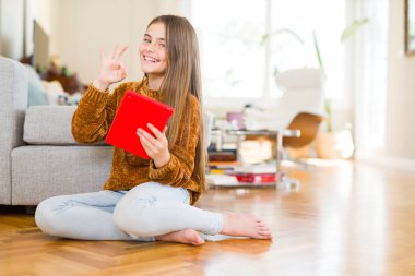 Güzel genç kız çocuk parmak ile ok işareti yapıyor katta oturan dijital Touchpad tablet kullanarak, mükemmel sembolü