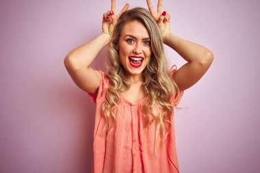 Pembe izole arka planda ayakta t-shirt giyen genç güzel kadın Bunny kulakları olarak kafa üzerinde parmak ile komik ve deli poz, neşeli gülümseyen