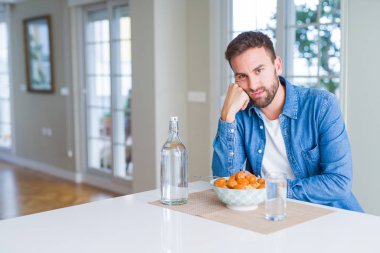 Handsome man eating pasta with meatballs and tomato sauce at home thinking looking tired and bored with depression problems with crossed arms. clipart