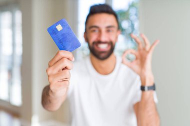 Yakışıklı İspanyol adam tutan kredi kartı parmaklar ile ok işareti yapıyor, mükemmel sembolü