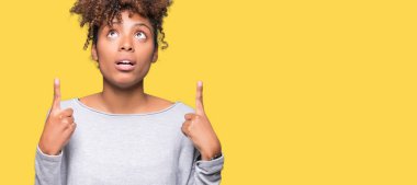 İzole arka plan güzel genç Afro-Amerikan kadın hayrete ve yukarıya bakıyor ve parmakları ile işaret ve silah kaldırdı şaşırttı.