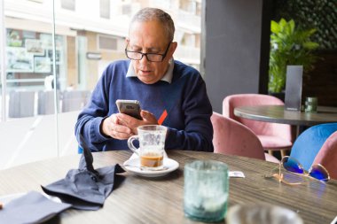 Mutlu ve zevk rahatlatıcı smartphone kullanarak emeklilik gülümseyen restaurante, kahve içme yakışıklı orta yaş komuta sizde