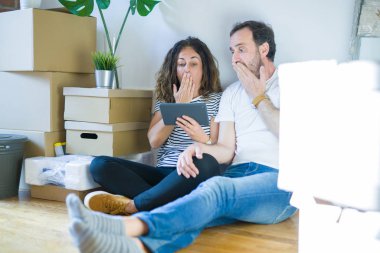 Orta yaş Senior çift yeni bir ev ile tablet kapağı ağız ile el hata için utanç, korku ifadesi, sessizlik, gizli kavramı korkuyor ifade kullanarak hareket