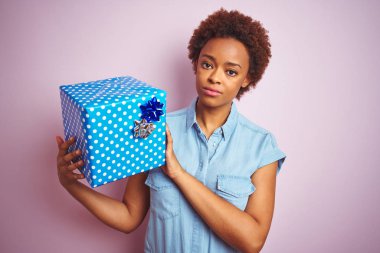 Afrika Amerikan kadın akıllı yüz düşünme ciddi üzerinde güvenli bir ifade ile pembe izole arka plan üzerinde Doğum günü hediyesi tutarak
