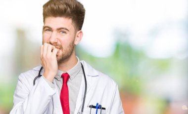 Genç yakışıklı Doktor adam stresli ve gergin elle çivi ısırma ağzına seyir tıbbi bir palto giyiyor. Anksiyete sorunu.