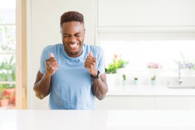 Yakışıklı afro-amerikan adam evde rahat t-shirt giyen kollar ile başarı için heyecanlı zafer gülümseyerek kutluyor kaldırdı. Kazanan kavramı.