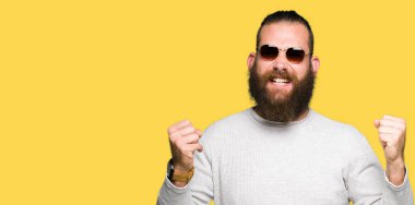 Gülümseyen ve başarı için çığlık çok mutlu ve heyecanlı kaldırdı, silah ile kazanan jest yapıyor güneş gözlüğü takmış genç yenilikçi bir adam. Kutlama kavramı.