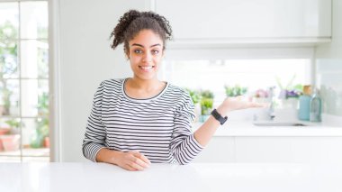 Afro saç ile güzel Afrikalı Amerikan kadın Casual çizgili kazak gülümseyen neşeli sunan ve kamera bakarak el avuç ile işaret giyiyor.