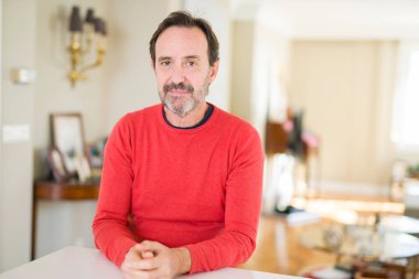 Yüzünde ciddi bir ifade ile yakışıklı orta yaş erkek evde. Basit ve doğal kameraya bakıyor.