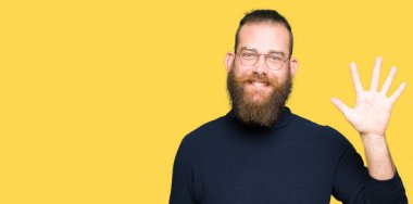 Genç sarışın adam gözlük ve balıkçı yakalı kazak gösteren ve parmak sayısı beş ile işaret kadar güven ve mutlu gülümseyen.