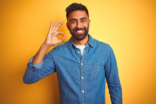孤立した黄色の背景の上に立つデニムシャツを着た若いインド人男性は 手と指でOkサインをやって肯定的に微笑んでいます 成功した式 — ストック写真