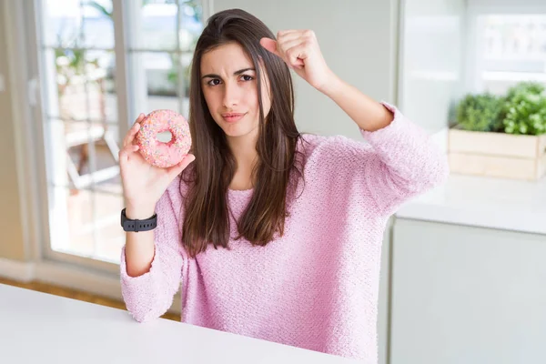 ピンクのチョコチップを食べる美しい若い女性ドーナツは怒り 狂気と上げられた手で叫んでイライラし 怒りの概念 — ストック写真