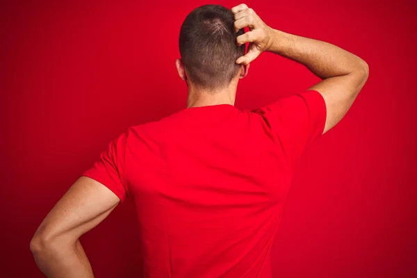 年轻的帅哥穿着休闲T恤在红色孤立的背景向后思考怀疑与手在头上 — 图库照片