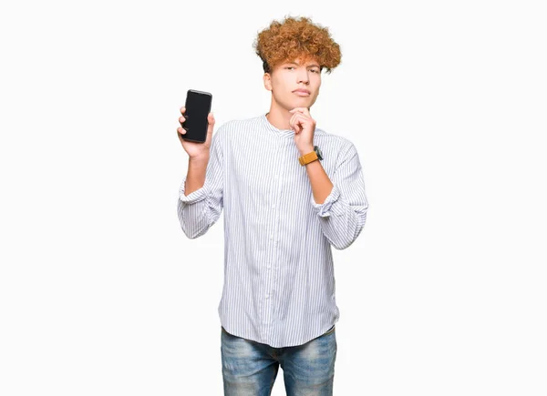 Jonge Knappe Man Toont Smartphone Scherm Ernstig Gezicht Denken Vraag — Stockfoto