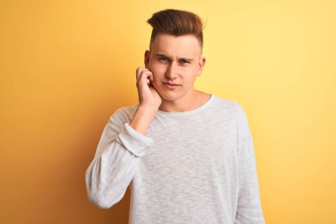 Genç yakışıklı adam beyaz rahat t-shirt giyen izole sarı arka plan üzerinde diş ağrısı veya diş üzerinde diş hastalığı nedeniyle ağrılı ifade ile el ile ağız dokunmadan ayakta. Diş hekimi konsepti.