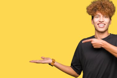 Siyah t-shirt giyen afro saç ile genç yakışıklı adam hayran ve kamera gülümseyen el ile sunmak ve parmak ile işaret.