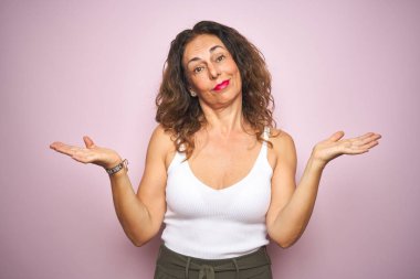 Orta yaş kıdemli kadın pembe izole arka plan clueless ve kollar ve elleri ile karıştı ifade üzerinde ayakta kaldırdı. Şüphe kavramı.