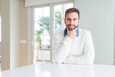 Rahat kazak giyen yakışıklı adam çapraz kolları ve çene üzerinde kaldırdı el ile gülümseme ile kameraya emin bakıyor. Olumlu düşünme.