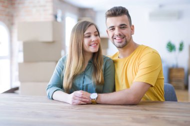 Evde masada oturan genç güzel çift, onların arkasında karton kutular ile yeni eve hareket için çok mutlu aşık sarılmak