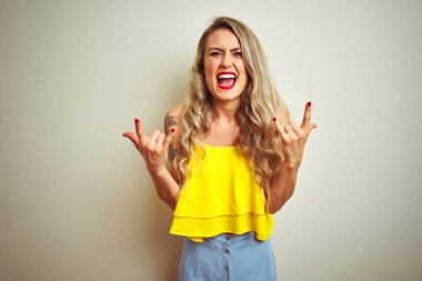 Beyaz izole arka plan üzerinde ayakta sarı t-shirt giyen genç güzel kadın elleri ile kaya sembolü yapıyor deli ifade ile bağırıyor. Müzik yıldızı. Ağır kavram.